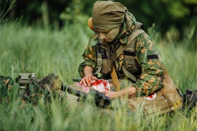 Military personnel applying wound dressing to wounded in the field.